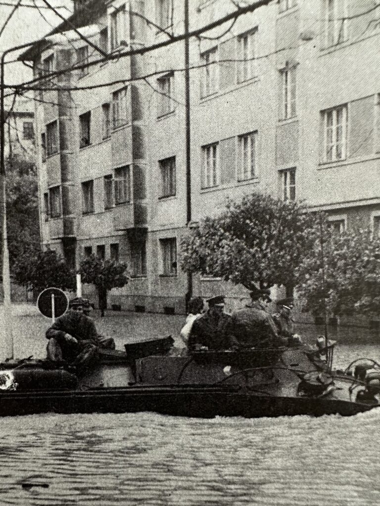 flooded residential street with military personnel in a boat aiding flood victims